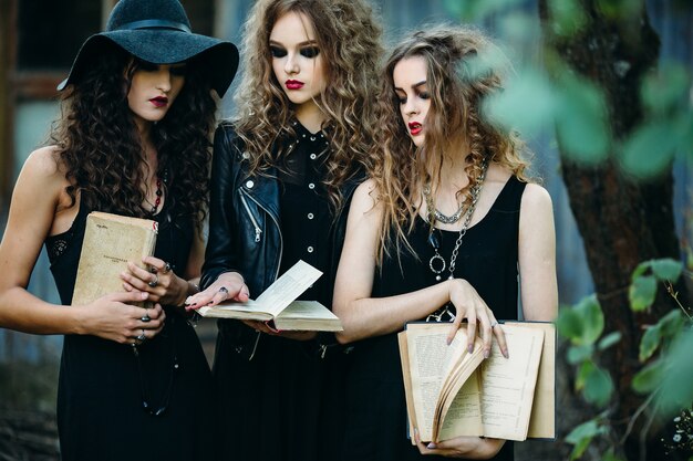 Girls disguised as witches holding open old books in hands