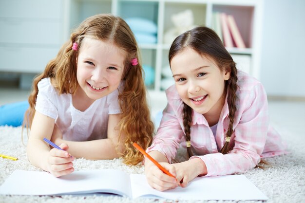 Girls drawing with pencils lying on floor