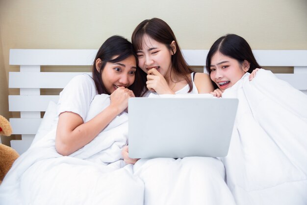 Girls group joyful looking movie on laptop together in bedroom