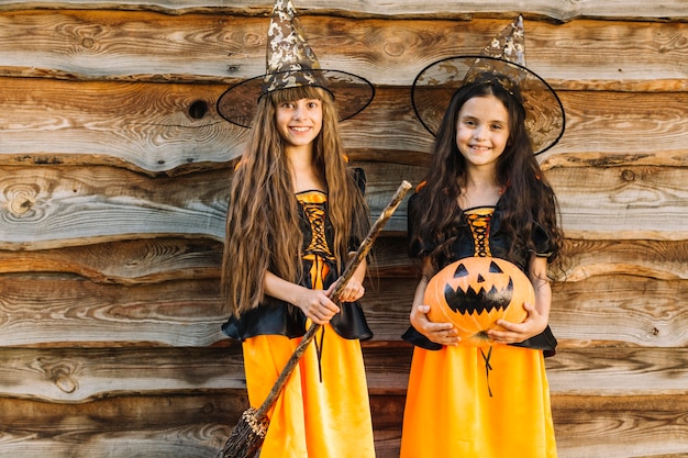 Foto gratuita ragazze in costumi di halloween con scopa e zucca guardando la fotocamera