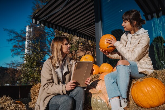 Girls have fun among pumpkins and haystacks on a city street. A beautiful young girls sitting on hay stacks. The concept of rural areas in a modern city. Photo Zone