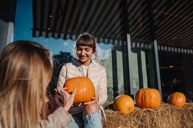 Girls have fun among pumpkins and haystacks on a city street