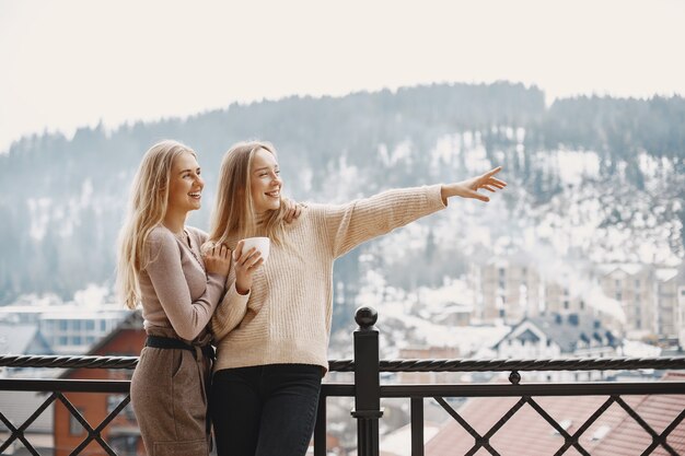 Girls in light clothes. Winter coffee on balcony. Happy women together.