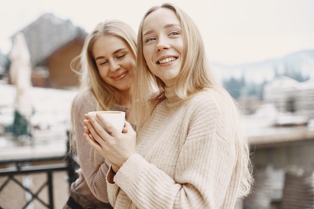 Girls in light clothes. Winter coffee on balcony. Happy women together.