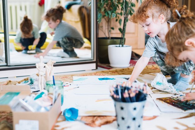 Girls painting on floor between box, pencils and papers