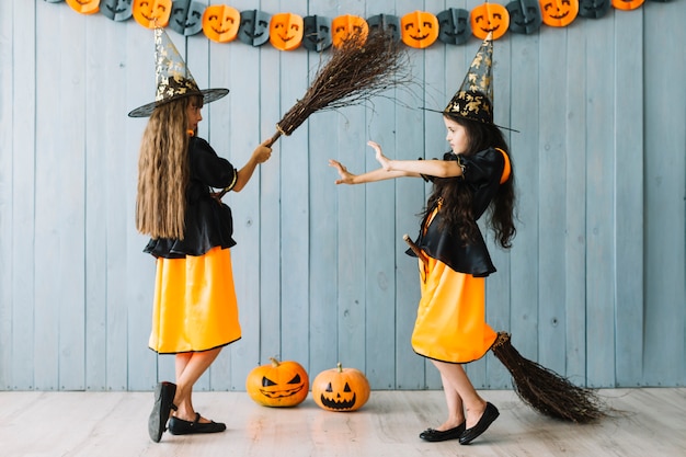 Free photo girls in pointy hats with brooms pretending fighting