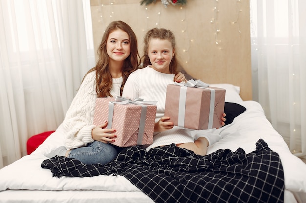 Девушки сидят на кровати. Женщины с подарком. Красавицы готовятся к Рождеству