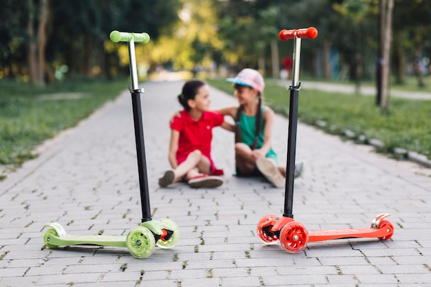 公園の歩道にプッシュスクーターの後ろに座っている女の子