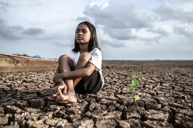 Girls sitting hugging their knees, looking at the sky and having trees on dry ground