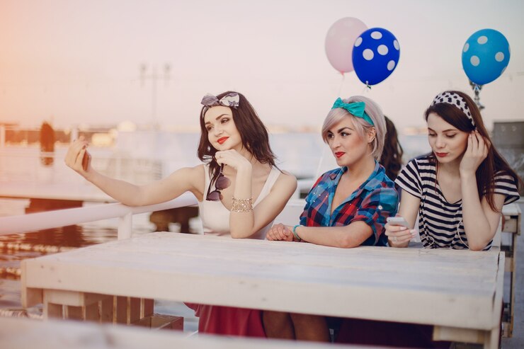 Free Photo girls sitting at a table doing a selfie with balloons behind
