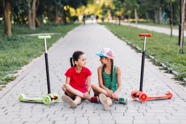 公園の歩道にプッシュスクーターで歩道に座っている女の子