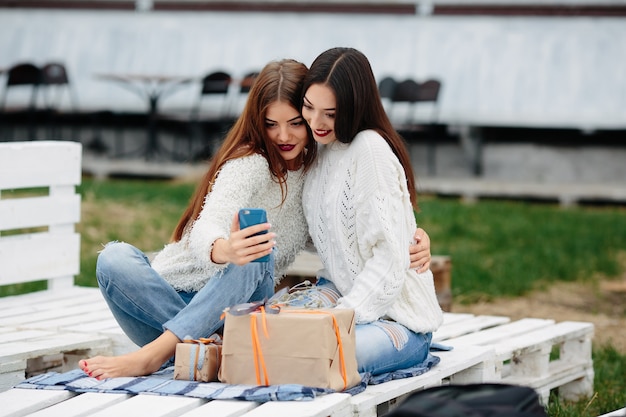 Girls sitting on a white wooden pallet with a gift looking at a mobile