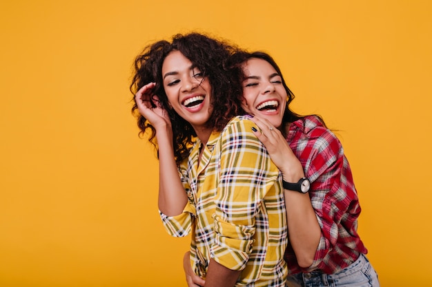 Girls in stylish street clothes sincerely laugh at each other's jokes. Girlfriends happily pose for common photo.