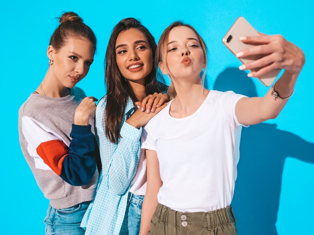 Девушки, делающие фотографии автопортрета селфи на смартфоне. Модели, позирующие около синей стены в студии. Женщина, делающая лицо утки на фронтальной камере