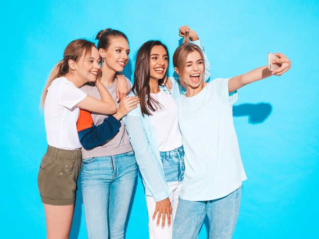 Girls taking selfie self portrait photos on smartphone.Models posing near blue wall in studio,Female showing positive face emotions