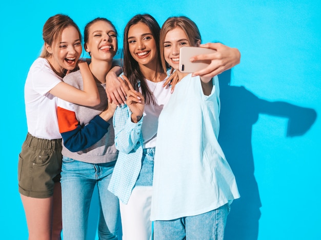 Girls taking selfie self portrait photos on smartphone.Models posing near blue wall in studio,Female showing positive face emotions