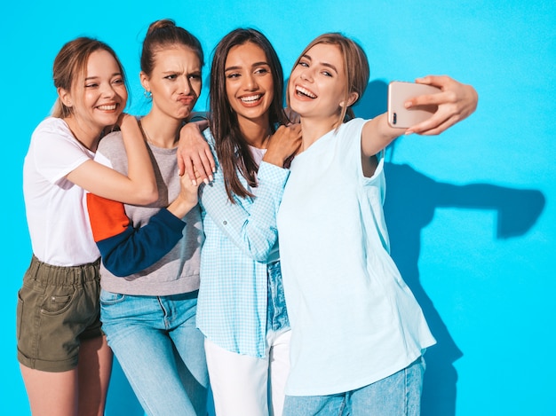 Ragazze che prendono le foto dell'autoritratto del selfie sullo smartphone modelli che posano vicino alla parete blu in studio, femmina che mostra le emozioni positive del fronte