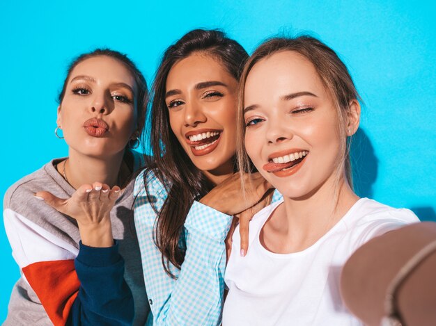 Girls taking selfie self portrait photos on smartphone.Models posing near blue wall in studio.