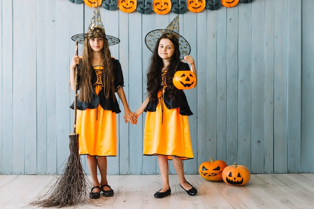 Girls in witch apparel standing with broom and holding hands 