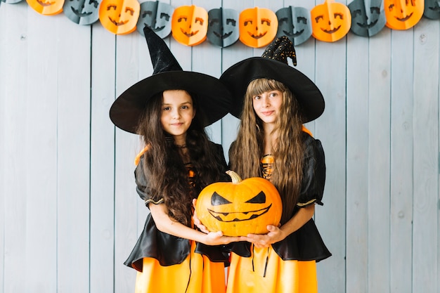 Girls in witch costumes holding pumpkin together