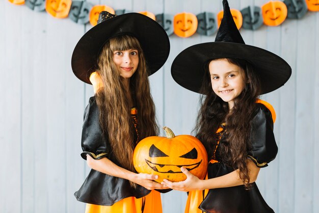 Girls in witch costumes holding pumpkin together