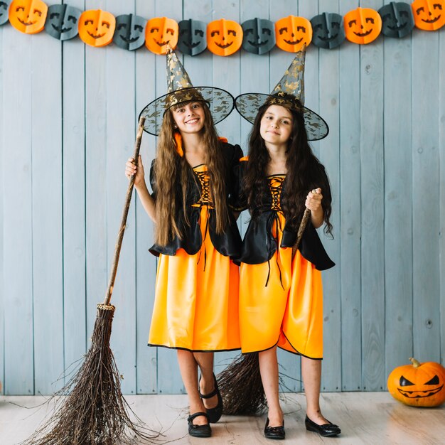 Girls in witch costumes hugging and holding broomsticks