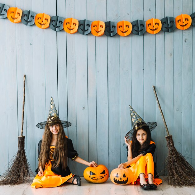 Girls in witch costumes and pointy hats sitting by fence