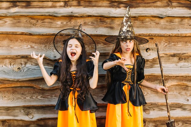 Girls in witch costumes posing and making faces on wood background