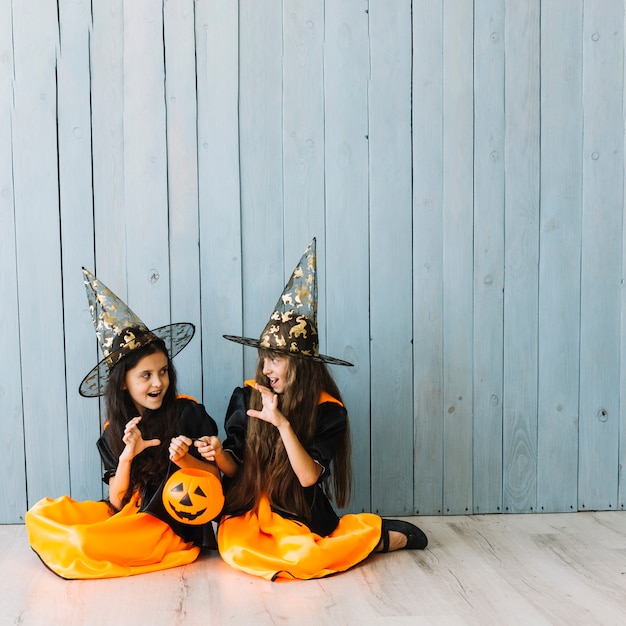 Girls in witch costumes sitting on floor doing scary gestures