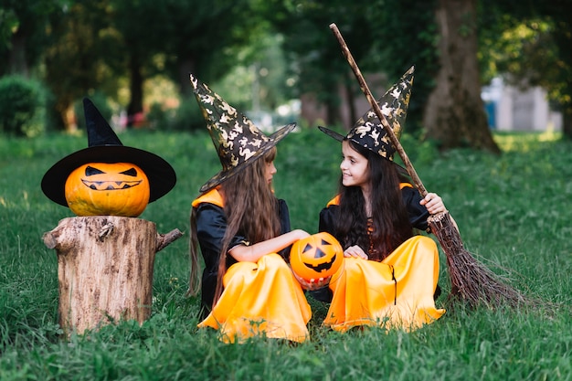 Girls in witch costumes sitting on grass, looking at each other