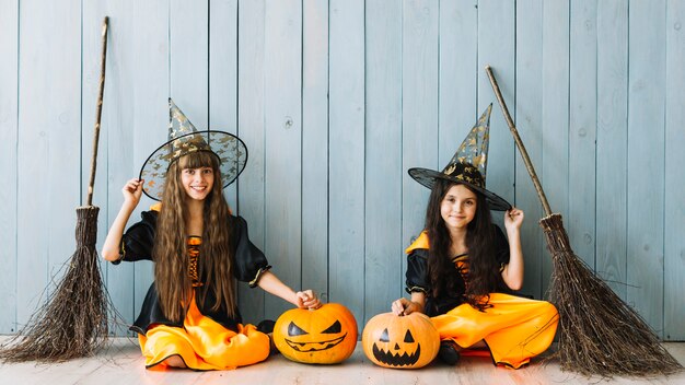 Girls in witch costumes sitting with pumpkins and brooms
