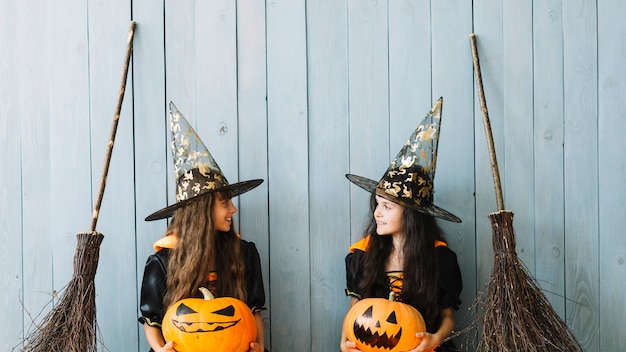 Girls in witch suits holding orange pumpkins and looking at each other