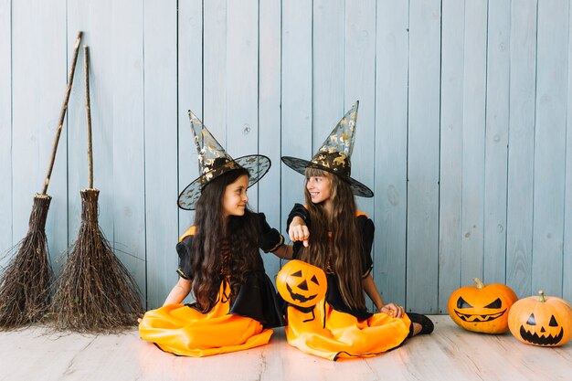 Girls in witch suits and pointy hats holding Halloween basket sitting on floor