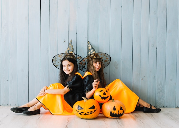 Girls in witch suits and pointy hats sitting on floor with pumpkins