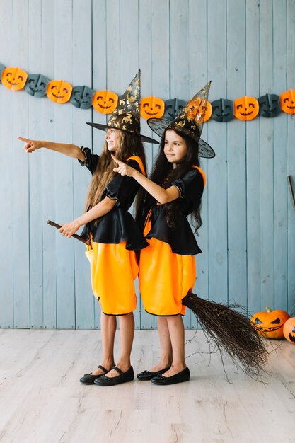 Girls in witch suits sitting on broom pointing away