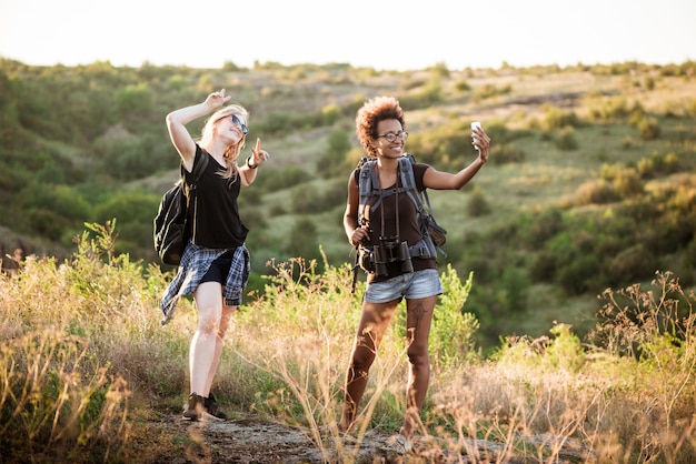 Free photo girls with backpacks smiling, making selfie, traveling in canyon