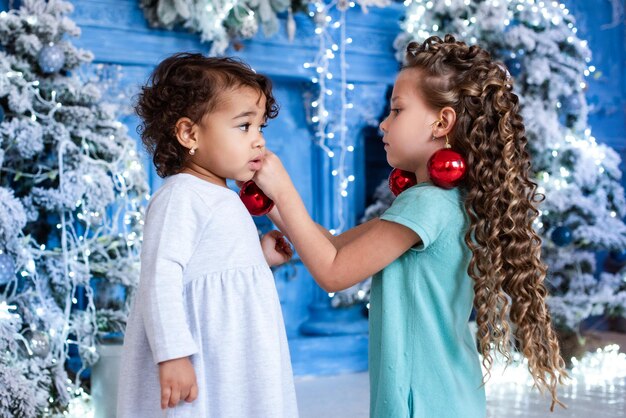 Girls with dark and light skin color are playing under the christmas tree. cute baby, african girl.