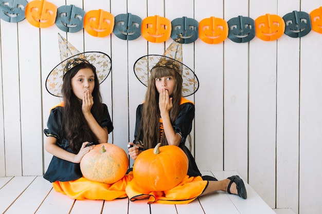 Girls with Halloween pumpkins closing mouth with hand