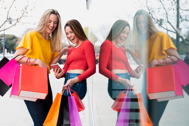 Free photo girls with shopping bags looking at phone near window