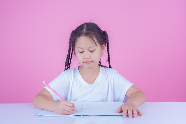 女の子はピンク色の背景に本を書きます。