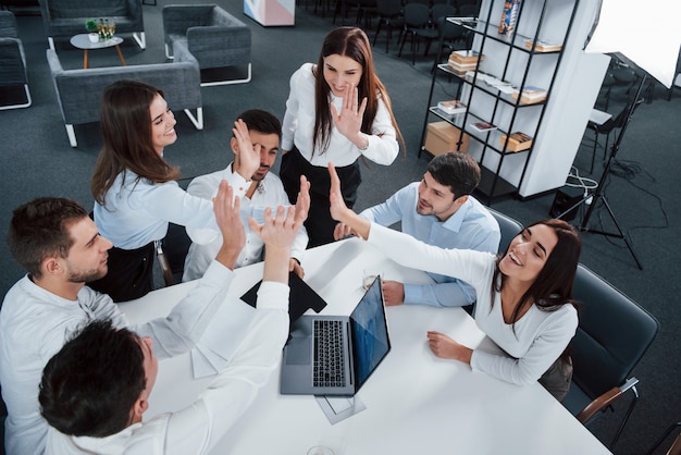 Giving high five to each other. Top view of office workers in classic wear sitting near the table using laptop and documents