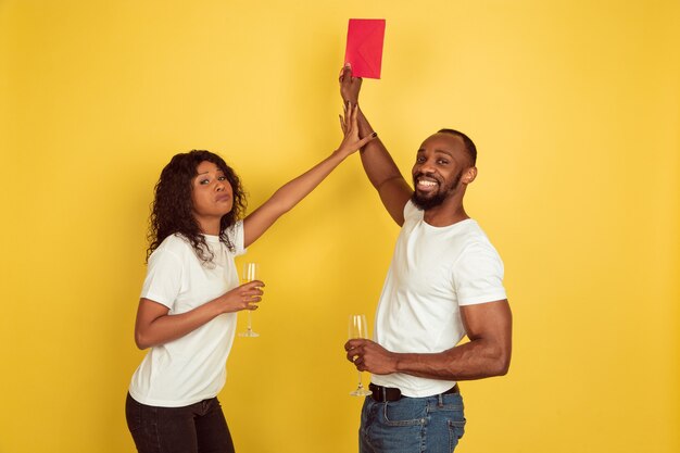 Giving red envelope. happy african-american couple isolated on yellow  wall. Concept of human emotions, facial expression, love, relations, romantic holidays.