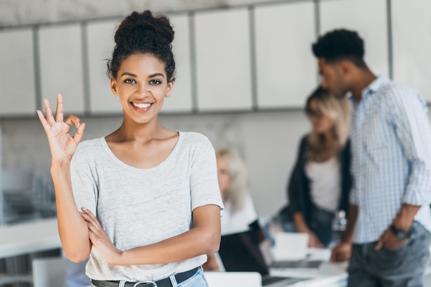 Glad african office worker with light-brown skin showing okay sign after conference with foreign partners. Portrait of female black freelancer enjoying successful project.