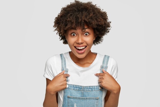 Glad amazed woman with dark skin points at herself with both index fingers