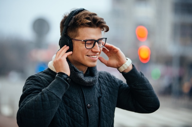 Glad attractive man listening to music in headphones, enjoying, walking on the street.