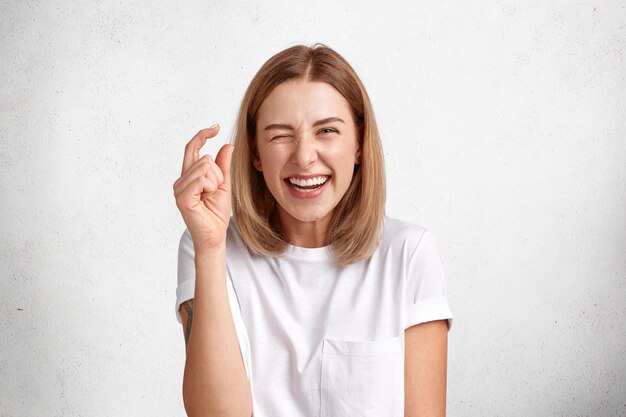 Free photo glad beautiful positive woman with stylish bobbed hairstyle, gestures in studio and shows size of something little, dressed casually.