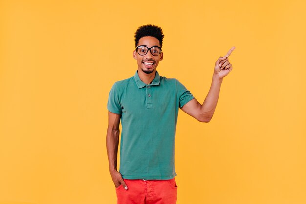 Glad boy in green t-shirt posing with pleasure. Indoor photo of laughing man in trendy outfit expressing positive emotions.