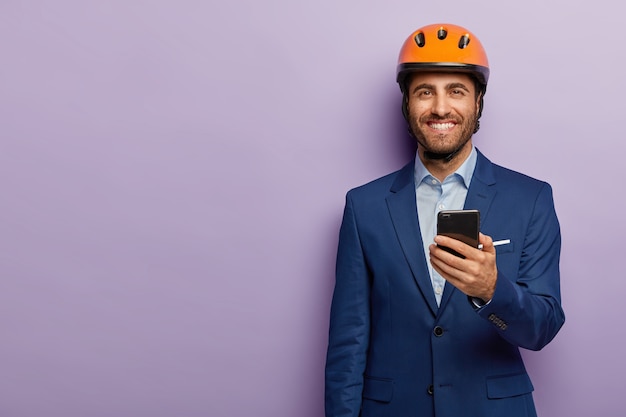 Glad businessman posing in classy suit and red helmet at the office