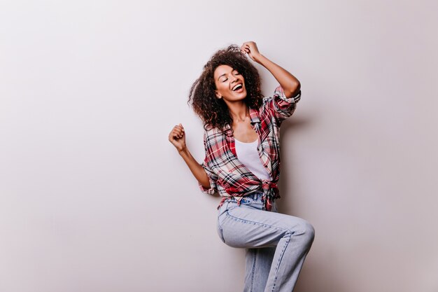 Рад танцевать смех африканской женщины. Красивая девушка в винтажных джинсах, охлаждая на белом.