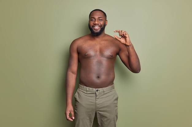 Glad dark skinned man poses with bare torso shapes little gesture